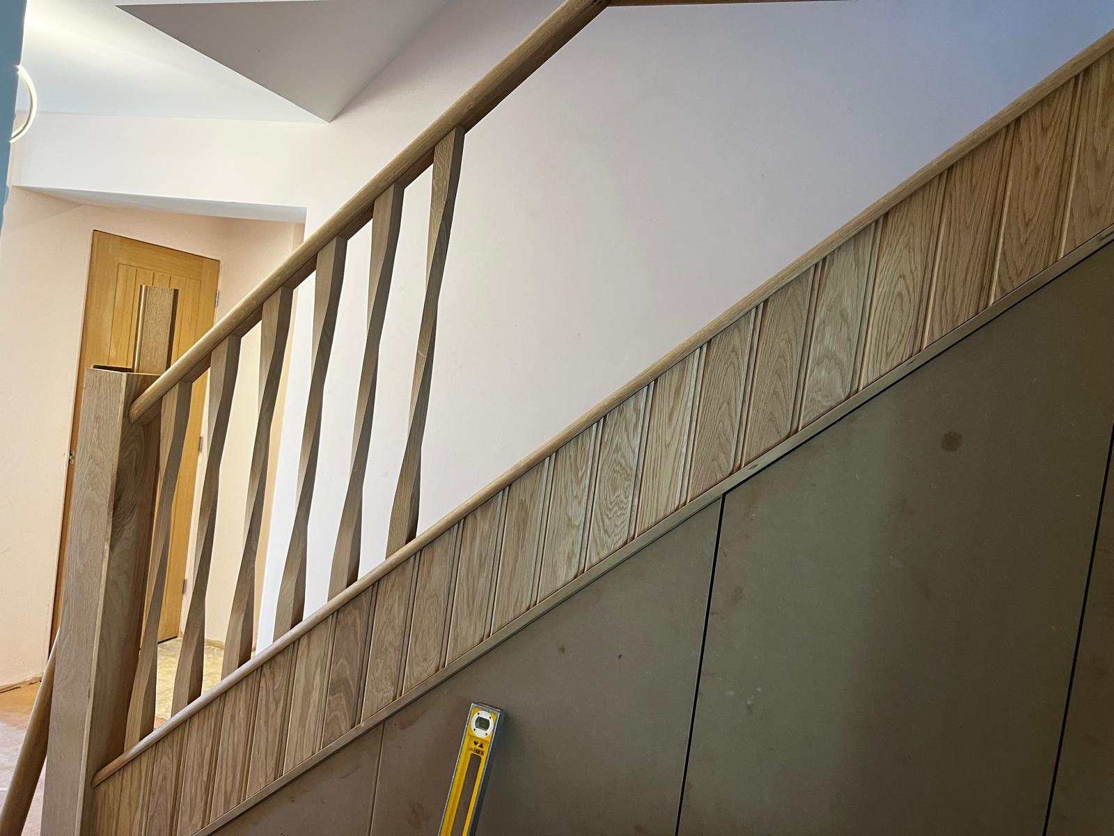 Bespoke oak staircase with wave-profile spindles and panelled understair storage